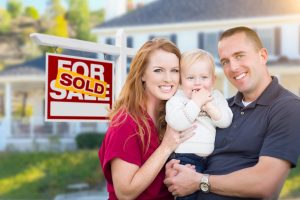 couple holding son in front of home with moving sign